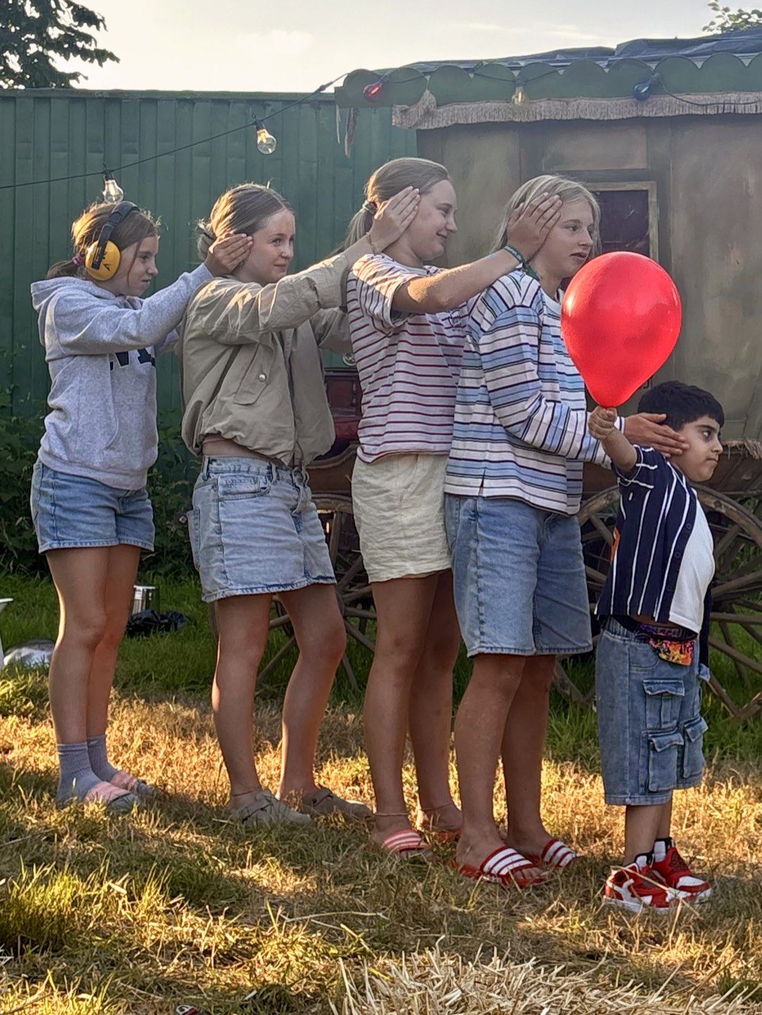 Børn på række holder for ørerne, mens en dreng holder en rød ballon